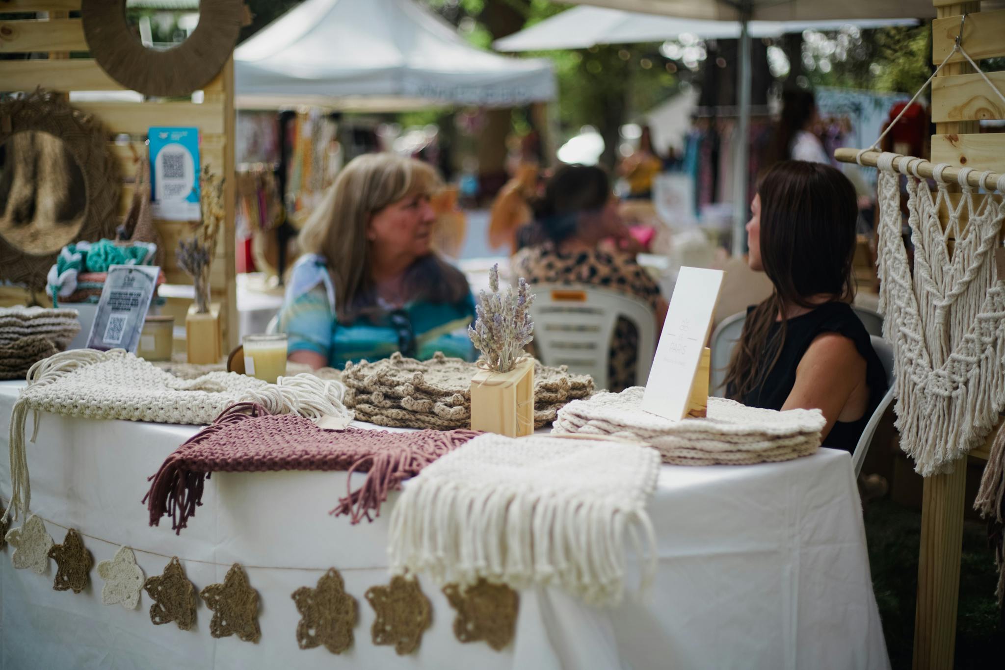 A vibrant street market scene displaying handmade woolen crafts with two women interacting.